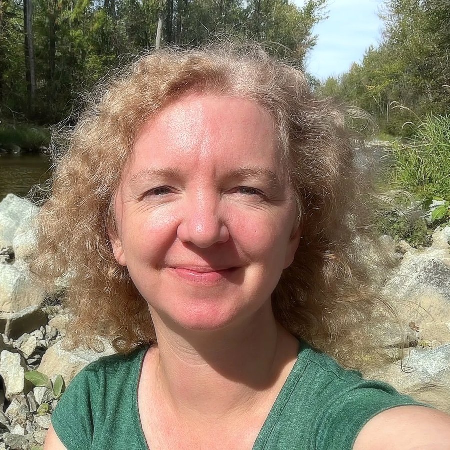 ML Villers smiling by a river in the forest